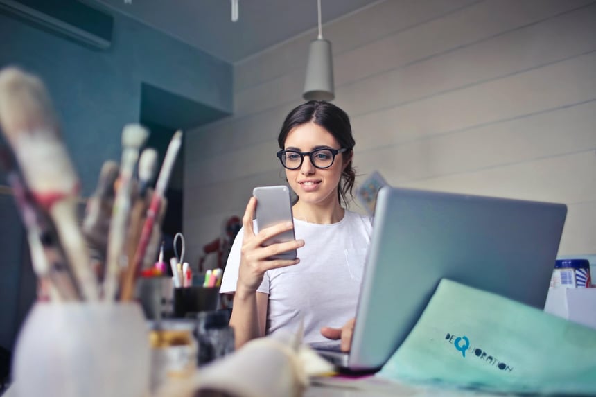 girl looking at cell phone from behind laptop